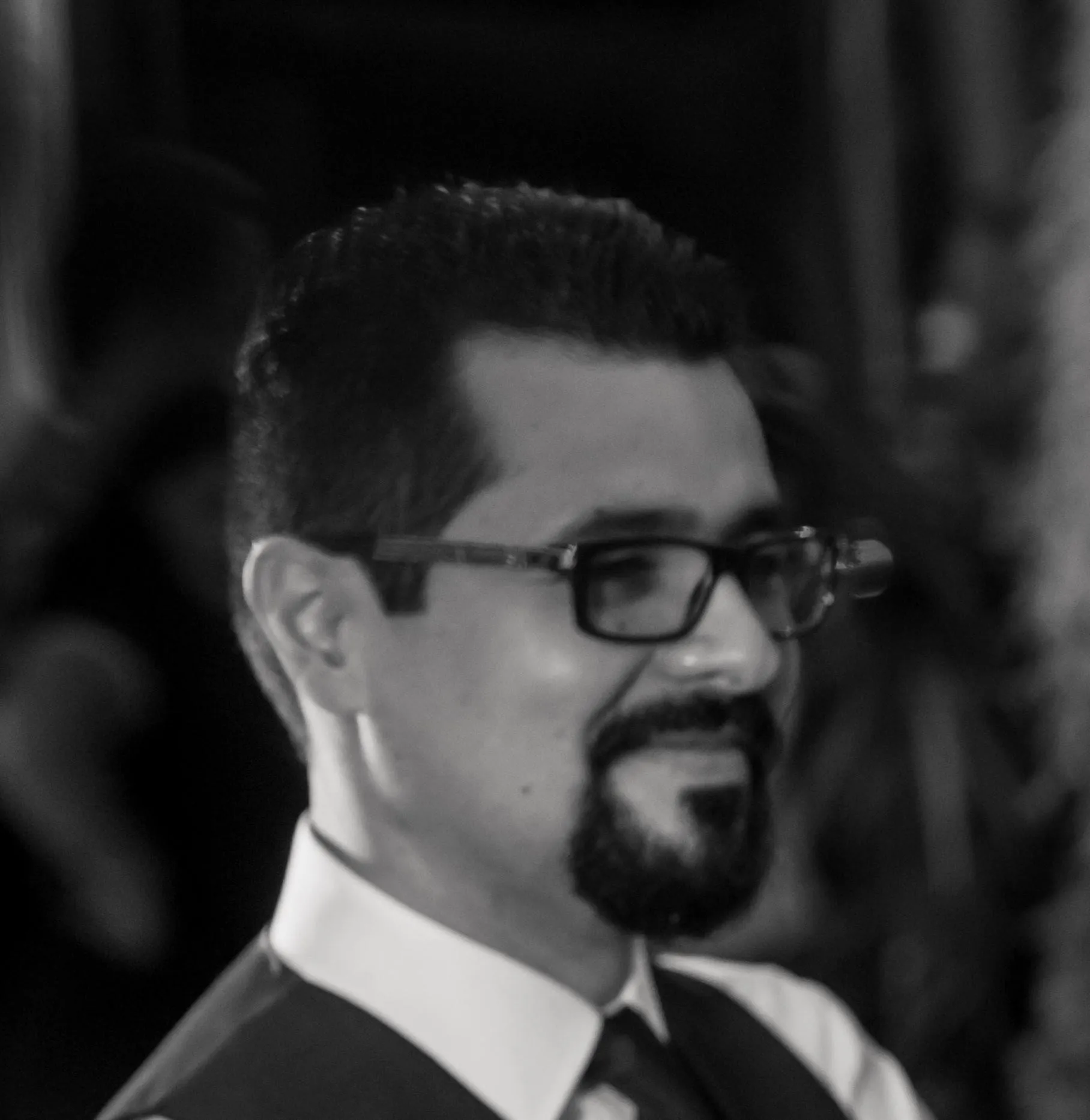 Israel, in profile, smiling, wearing glasses and a shirt and tie.